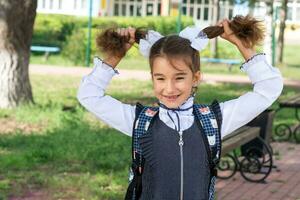 allegro divertente ragazza con un' sdentato Sorridi nel un' scuola uniforme con bianca fiocchi nel scuola cortile. indietro per scuola, settembre 1. contento allievo con un' zaino. primario formazione scolastica, elementare classe. foto