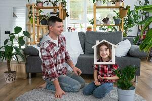 incompleto famiglia papà e figlia siamo godendo nuovo casa, seduta su divano. mutuo, assicurazione e protezione, acquisto e in movimento in il tuo proprio casa, verde Casa con in vaso pianta foto