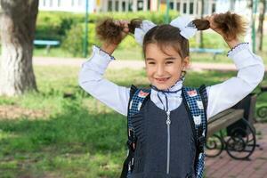 allegro divertente ragazza con un' sdentato Sorridi nel un' scuola uniforme con bianca fiocchi nel scuola cortile. indietro per scuola, settembre 1. contento allievo con un' zaino. primario formazione scolastica, elementare classe. foto