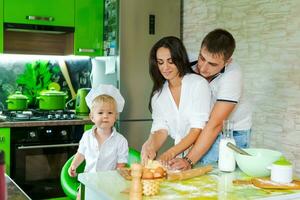 contento famiglia mamma e poco figlio e papà siamo preparazione Impasto nel cucina a tavolo. prodotti per Impasto siamo su tavolo foto