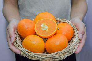 mano Tenere un' di legno cestino pieno con parecchi arance, tagliare nel metà per svelare il semi dentro. naturale vitamine foto