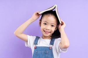 ritratto di bambino asiatico che tiene libro su sfondo viola foto