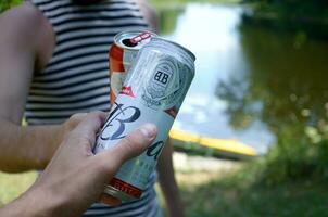 giovane uomo aumentare budweiser germoglio birra può con maschio amico su sfocato fiume con kayak e alberi foto