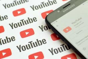 Youtube App su Samsung smartphone schermo su carta bandiera con piccolo Youtube loghi e iscrizioni. Youtube è Google filiale e americano maggior parte popolare condivisione video piattaforma foto