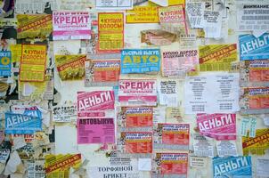 Kharkov, Ucraina - ottobre 2, 2019 grunge Messaggio tavola con molti annuncio. persone diffusione pubblicità e informazione su bianca carta di inviare esso su metallo recinto foto