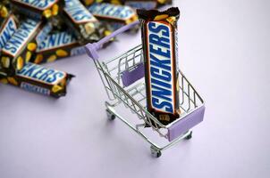 molti risatine cioccolato barre impilati vicino su con shopping carrello su leggero viola sfondo. risatine barre siamo prodotta di Marte incorporato foto