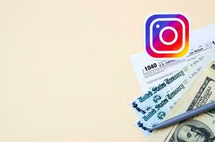 instagram stampato logo bugie con 1040 individuale reddito imposta ritorno modulo con rimborso dai un'occhiata e centinaio dollaro fatture su beige sfondo. Aiuto nel imposta periodo a partire dal sociale Rete concetto foto