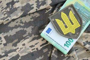 ucraino esercito simbolo e mazzo di Euro fatture su militare uniforme. pagamenti per soldati di il ucraino esercito a partire dal europeo unione, stipendi per il militare. guerra supporto foto