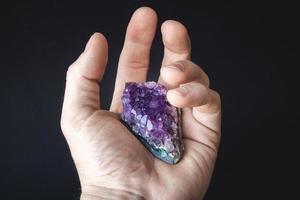 cristallo viola di ametista su un pezzo di roccia giace sul palmo della mano foto