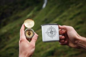 tè in una tazza di metallo turistica e una bussola in mano sfondo naturale