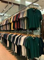 riga di alla moda polo magliette per uomo su di legno appendiabiti o cremagliera nel un' capi di abbigliamento boutique Al dettaglio negozio concetto di ai generato foto