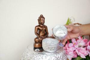 vicino su mano detiene tailandese tradizionale argento ciotola per versare acqua su il Budda statua su Songkran giorno per culto e rendere auguri per il prosperità. concetto, cultur di fede. religioso cerimonia per fortuna foto