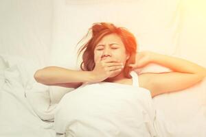 bella giovane donna assonnata che sbadiglia quando si sveglia la mattina foto