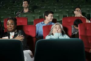 arioso persone nel Teatro. anziano asiatico donna e multirazziale pubblico siamo impaurito di Guardando thriller e orrore cinema, spaventato insieme di film, e divertimento stile di vita con film arte mostrare. foto