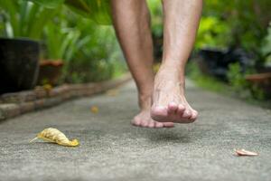 anziano uomo a piedi nudi a piedi su cemento passerella nel il giardino foto