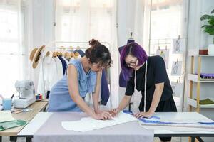 giovane fiducioso femmina progettista nel viola colore capelli discutere di Abiti modello con sarto a moda studio, concetto di business,industria,design,sartoria foto