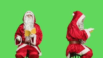santo nick legge conferenza romanzo su sedia, uomo vestito come Santa Claus con rosso completo da uomo e bicchieri mentre lui è lettura letteratura libro al di sopra di schermo verde. persona nel costume godendo fiaba finzione. foto