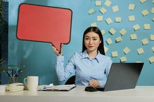 femmina ufficio lavoratore Tenere discorso bolla per mostrare Messaggio su cartone isolato copyspace, pubblicità modello modello modello su cartone. aziendale dipendente a scrivania guardare a telecamera. foto