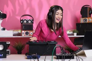 asiatico esecutore in piedi a dj tavolo miscelazione elettronico musica con techno utilizzando professionale giradischi, avendo divertimento nel studio al di sopra di rosa sfondo. musicista giocando stereo suoni con elettronica foto