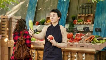 giovane commessa Tenere proprio prodotti su telecamera, presentazione naturale colorato localmente cresciuto produrre. giovane femmina fruttivendolo mostrando di stagione biologico eco frutta e verdure produrre. foto