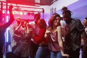 appassionato uomo e donna coppia danza insieme e in movimento per musica battiti nel discoteca. africano americano fidanzato e caucasico fidanzata partying su pista da ballo a discoteca foto