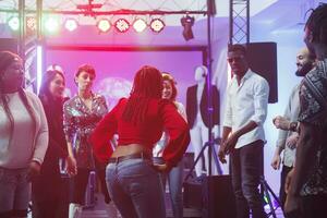 donna ballerino mostrando si sposta su pista da ballo per frequentatori di discoteche folla a discoteca nel discoteca. giovane africano americano ragazza festeggiare partying a improvvisato danza battaglia nel club foto