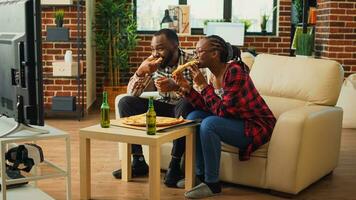 contento partner mangiare fette di Pizza su divano e abbuffata Guardando tv mostrare a casa, godendo veloce cibo pasto. moderno coppia ricevente porta via cibo ordine e seduta per avere cena a televisione. foto