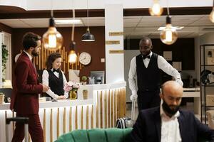 fattorino assistere uomo d'affari dopo dai un'occhiata in, fornire concierge Servizi nel lusso Hotel atrio. bianca collare lavoratore registrato a davanti scrivania ricezione, in viaggio all'estero per assistere incontri. foto