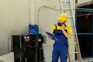 condito meccanico su il Telefono con cliente segnalazione trovato problemi su all'aperto HVAC sistema dopo completo ispezione. lavoratore andando al di sopra di aria condizionatore assicurazione dettagli con cliente mentre su chiamata foto