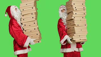 Santa Claus in posa con mucchio di Pizza scatole, trasporto enorme pila di consegna cibo, uomo indossare tradizionale personaggio completo da uomo con bianca barba e occhiali. persona nel costume al di sopra di schermo verde. foto