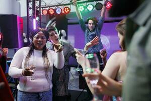 persone potabile alcol, danza e cantando a discoteca festa con vivere musica. allegro folla rilassante, godendo bevande e avendo divertimento su pista da ballo a sociale raccolta nel club foto