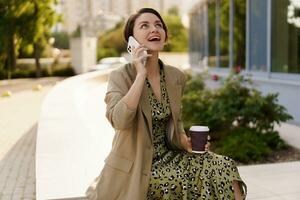 all'aperto foto di elegante bellissimo donna con corto taglio di capelli godendo autunno,n giorno Tenere tazza di caffè, utilizzando mobile Telefono. usurante casuale jacker e elegante vestire.