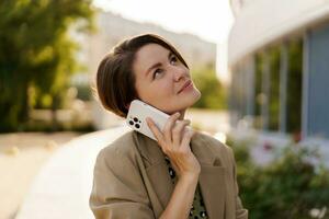 all'aperto foto di elegante bellissimo donna con corto taglio di capelli godendo autunno,n giorno Tenere tazza di caffè, utilizzando mobile Telefono. logorante casuale jacker e elegante vestire.