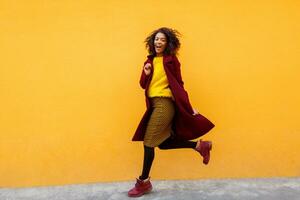 pieno lunghezza Immagine di eccitato nero donna salto con contento viso espressione su giallo sfondo. foto