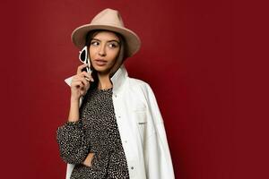 vicino su interno studio moda ritratto di bellissima donna nel elegante autunno bianca cappotto e beige cappello in posa su rosso sfondo. foto