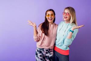 Due ragazze con sorpresa viso soggiorno al di sopra di viola parete. indossare alla moda felpe con cappuccio e freddo occhiali. foto