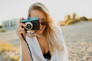elegante formoso ragazza con retrò telecamera in posa su soleggiato spiaggia. la libertà e viaggio concetto. foto