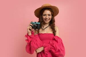 bella rosso testa femmina turista con telecamera. studio tiro di stupito donna Tenere blu retrò telecamera e in posa al di sopra di rosa sfondo. foto