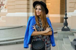 grazioso ragazza nel elegante autunno attrezzatura a piedi mentre vacanze nel Europa. elegante pelle Borsa. blu giacca e nero cappello. foto