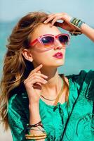 sbalorditivo colorato all'aperto estate ritratto di bella giovane bionda bellissimo donna nel freddo occhiali da sole in posa su il soleggiato tropicale spiaggia. foto
