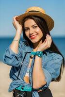 sorridente donna nel cannuccia cappello e elegante estate attrezzatura in posa con retrò telecamera su il spiaggia. foto