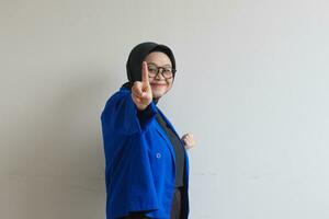giovane bellissimo asiatico musulmano donna, indossare bicchieri e blu blazer Esprimere a gesti numero 1 cartello mano con indice dito foto