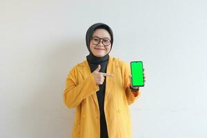 sorridente bellissimo asiatico donne nel giallo blazer e hijab mostrando verde schermo mobile Telefono foto