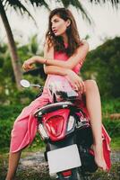 giovane elegante sexy bellissimo donna nel rosa vestito su scooter motocicletta tropicale vacanza foto