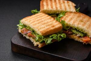 delizioso croccante Sandwich con pane abbrustolito, salmone, avocado, pomodori, sale, spezie e erbe aromatiche foto