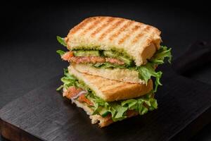 delizioso croccante Sandwich con pane abbrustolito, salmone, avocado, pomodori, sale, spezie e erbe aromatiche foto