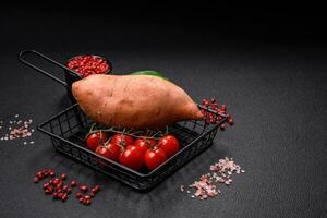 fresco grande rosa dolce Patata tuberi con pomodori e spezie su un' buio sfondo foto