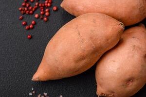 fresco grande rosa dolce Patata tuberi con pomodori e spezie su un' buio sfondo foto