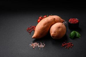 fresco grande rosa dolce Patata tuberi con pomodori e spezie su un' buio sfondo foto