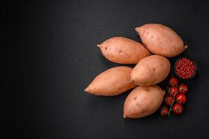 fresco grande rosa dolce Patata tuberi con pomodori e spezie su un' buio sfondo foto